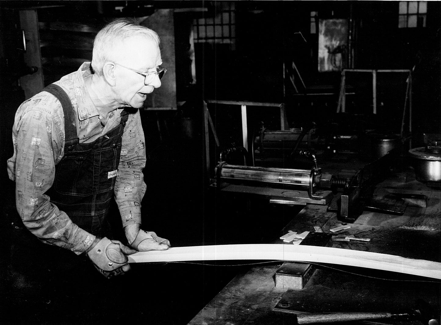Black and white photograph of a man working with wood in a workshop.